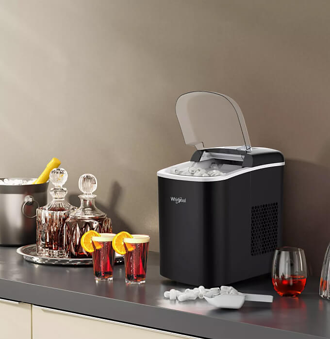 A Whirlpool® Ice Maker sitting on a counter with cold beverages placed next to it.