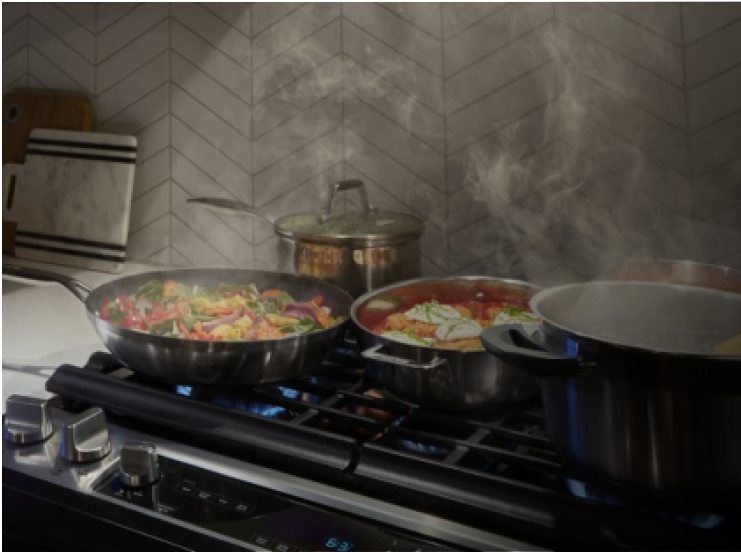 Multiple pans with food cooking in them on a gas cooktop