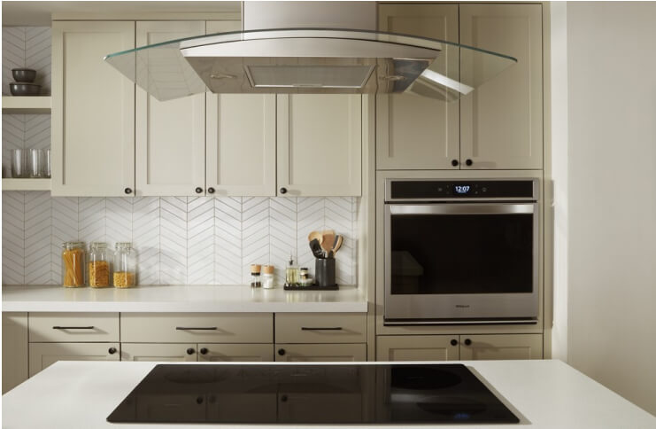 A Whirlpool® Wall Oven, Electric Cooktop and Island Mount Canopy Range Hood in a kitchen with light cabinets and a island