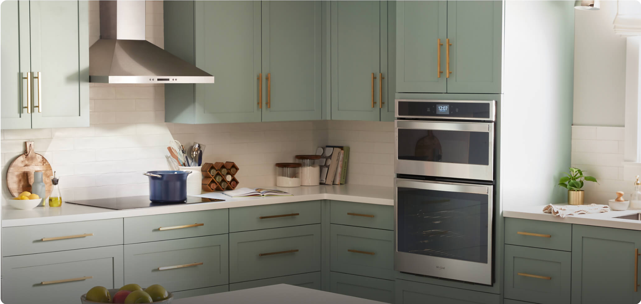 Whirlpool® Wall Oven Microwave Combination, Electric Cooktop and Wall Mount Range Hood in a kitchen with sage green cabinets