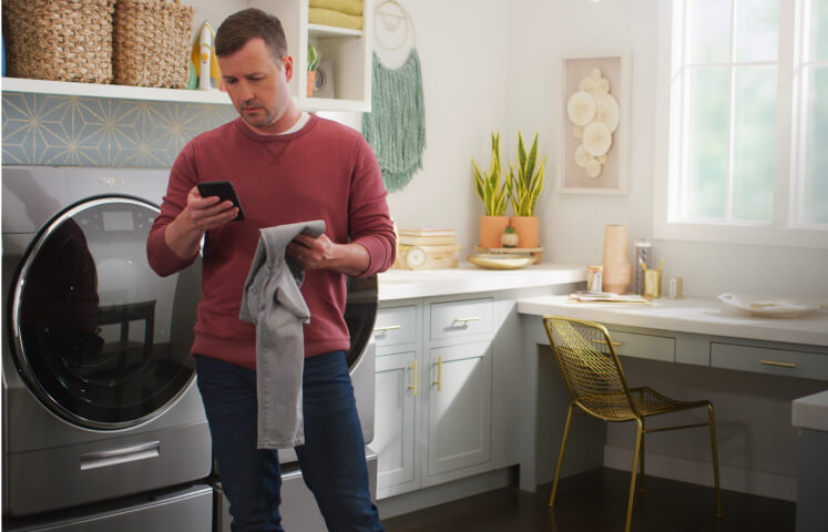  A man holding a smartphone in the laundry room with the home heartbeat blog logo