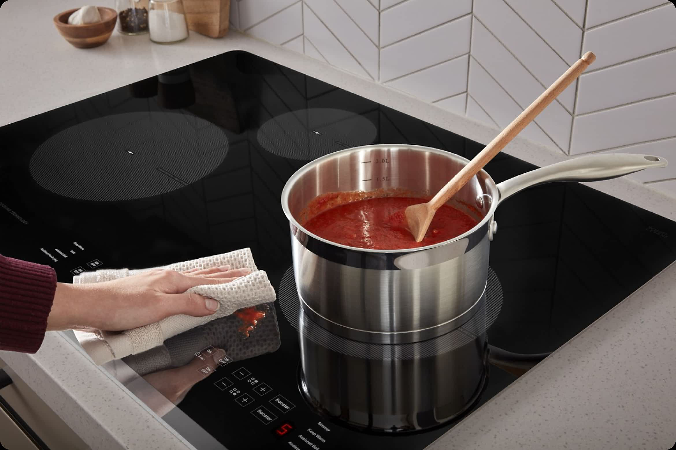 Hands wipe down a Whirlpool® Cooktop as sauce simmers
