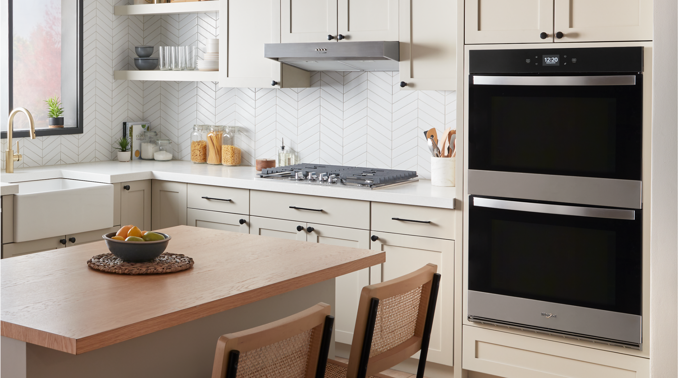 A Whirlpool® Smart Double Wall Oven, Gas Cooktop and Range Hood in a kitchen with light cabinets and an island