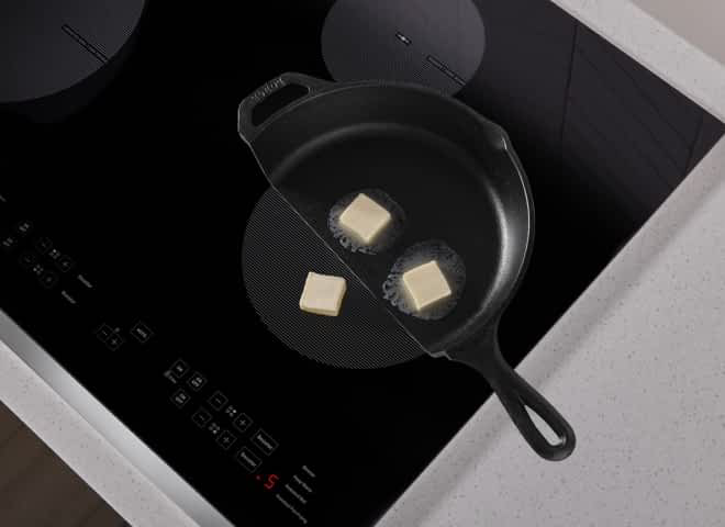 A frying pan cut in half on an induction cooktop, showing butter melting in the pan and not melting on the exposed element.