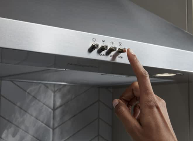 A hand pressing the venting button on a Whirlpool® Canopy Hood