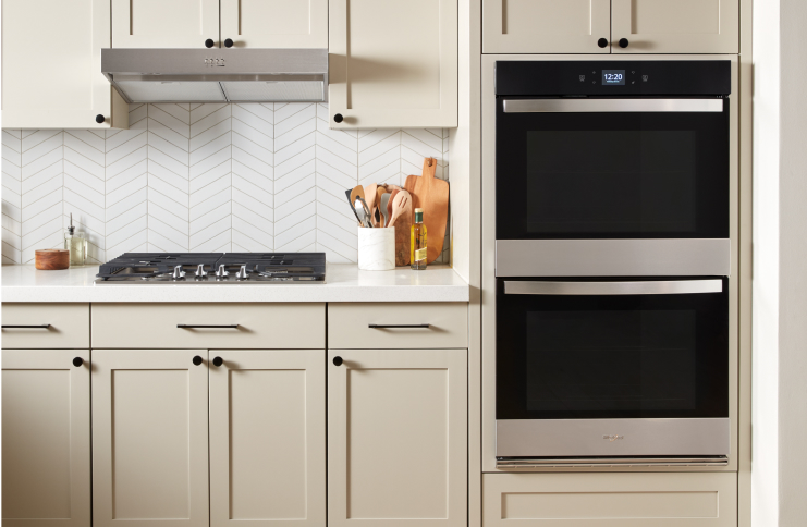 A Whirlpool® Double Wall Oven, Gas Cooktop and Undercabinet Range Hood in a kitchen with light cabinets