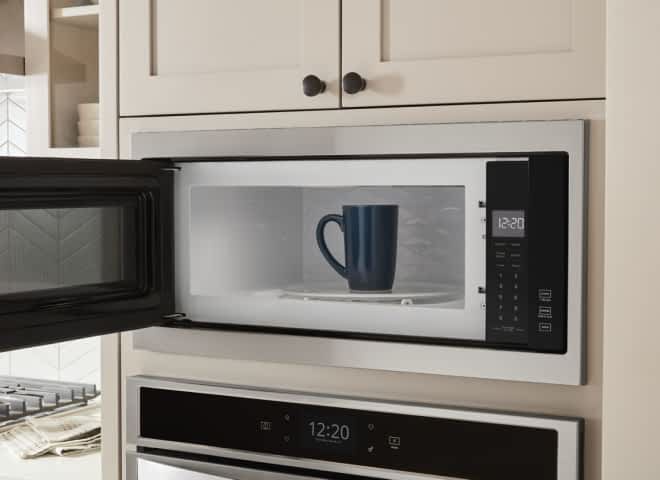 A coffee cup sits inside an open Whirlpool® Microwave