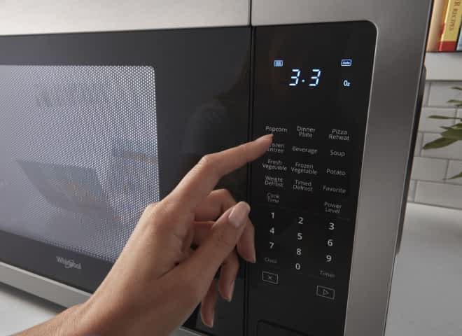 A hand presses a button on a Whirlpool® Microwave