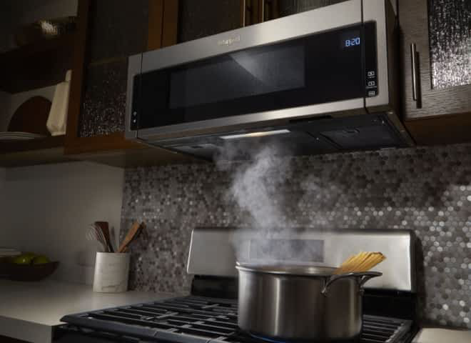 A steaming pot sits on the stove beneath a Whirlpool® Low Profile Over-The-Range Microwave