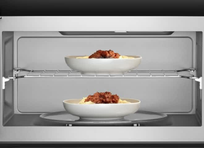 The inside of a microwave shows two large dishes on two separate racks.