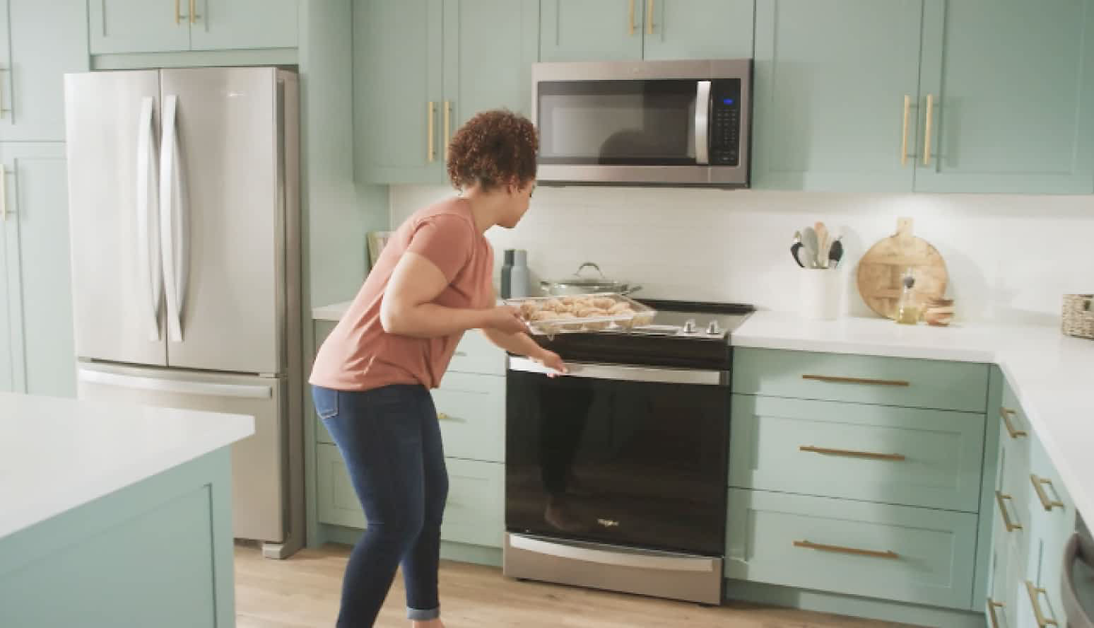 A woman puts a tray of chicken wings into a Whirlpool® Range with Air Fry Mode