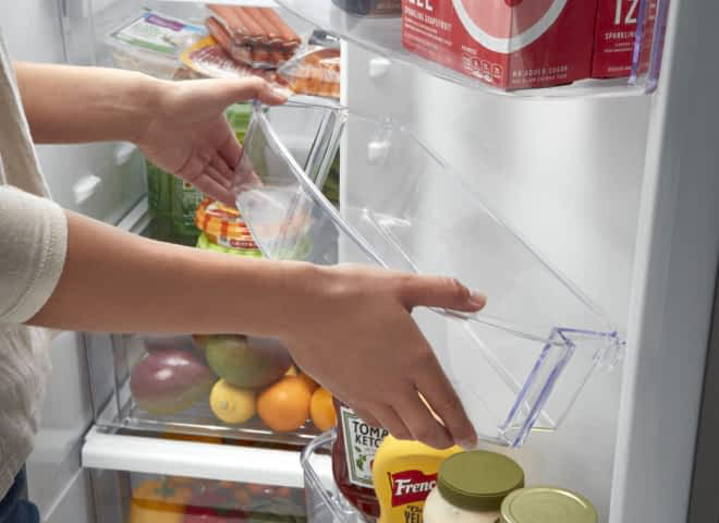 A woman moves the Adjustable Gallon Door Bin in a Whirlpool® Refrigerator