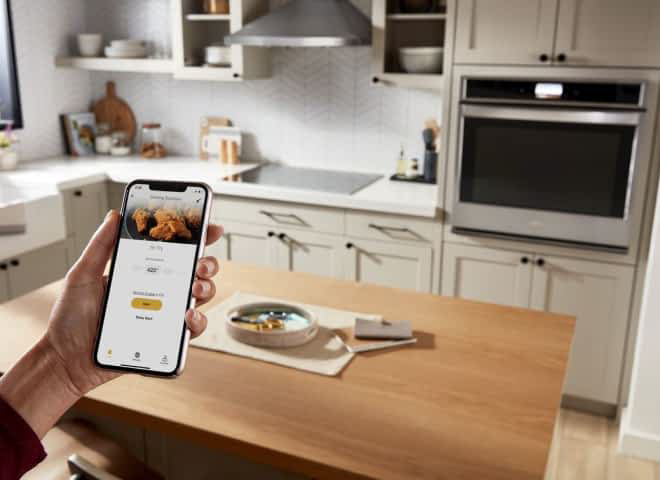 A hand holding a phone displaying the Whirlpool® App