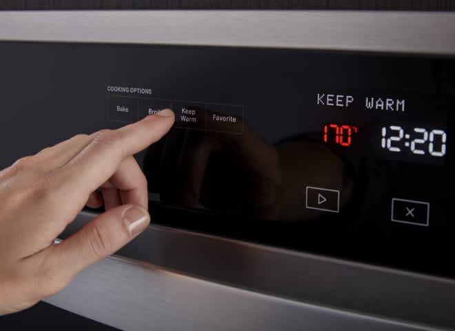 A hand presses the Keep Warm button on a Whirlpool® Wall Oven
