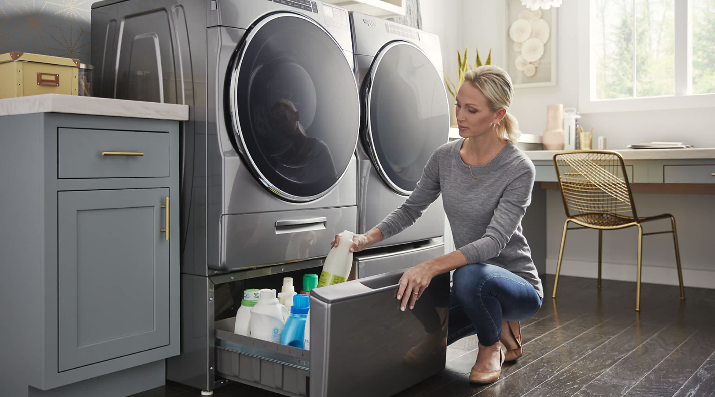 A woman puts detergent away in the pedestals under her Whirlpool® Front Load Washer & Dryer Set