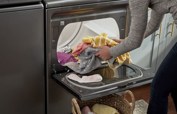 A person unloads laundry from a Whirlpool® Front Load Dryer