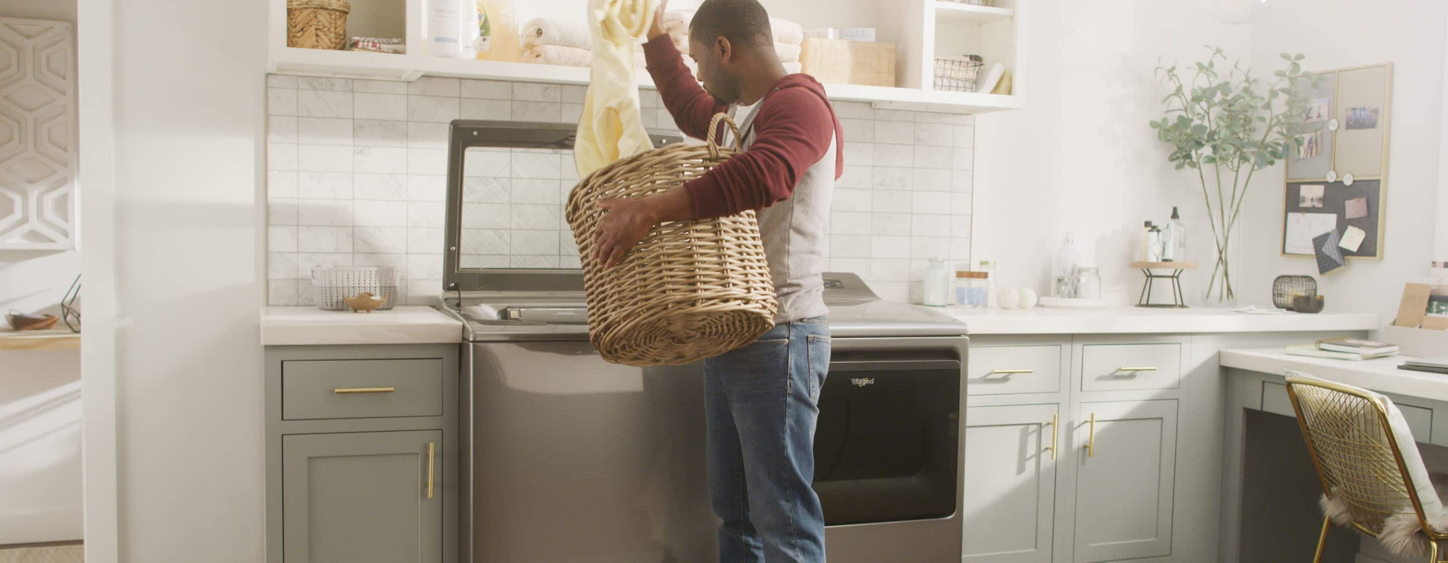 A man loads laundry in a Whirlpool® Top Load Washer and Dryer set