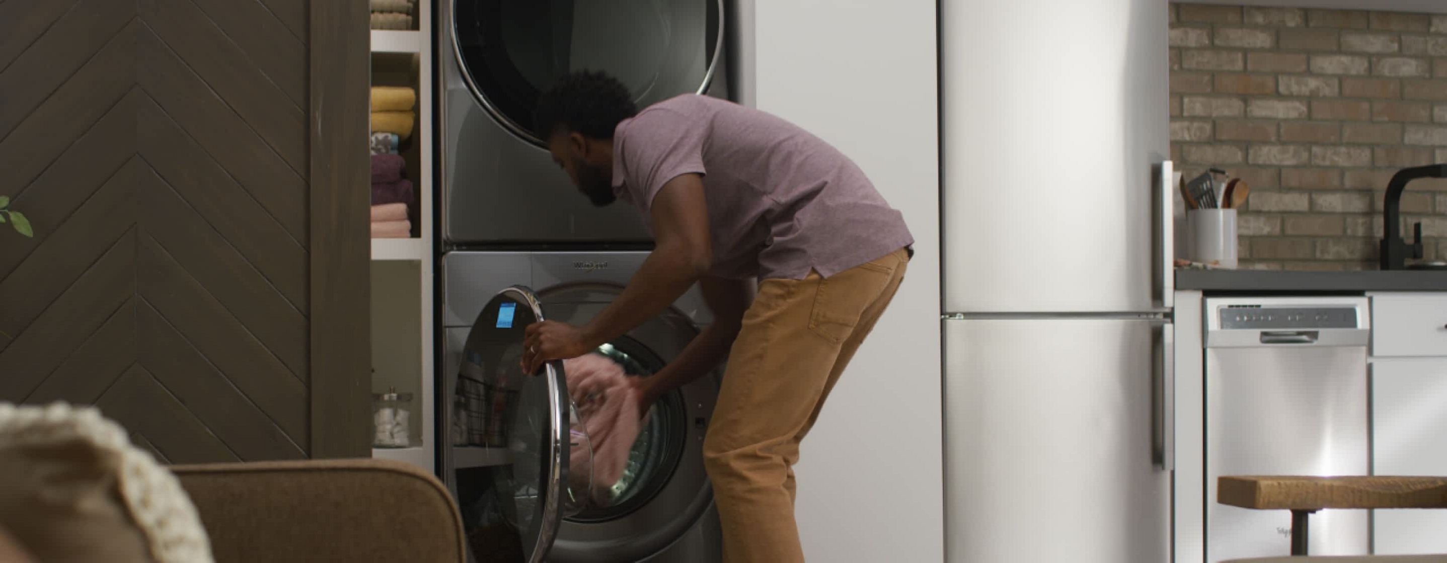 A man loads laundry into a Whirlpool® Stacked Washer & Dryer