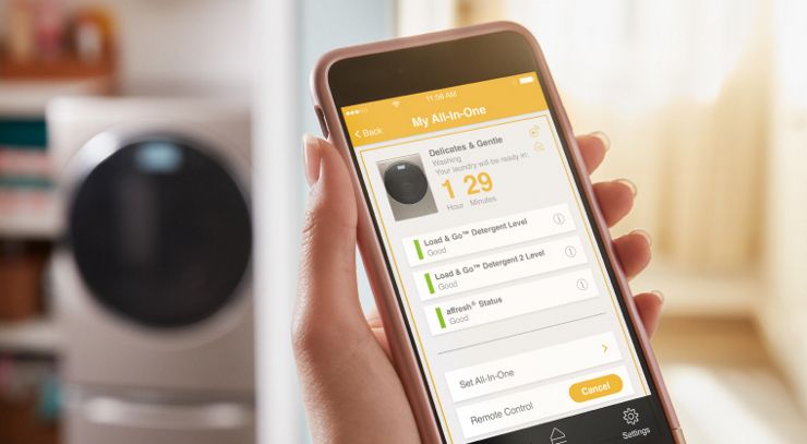 Un smartphone con la aplicación de Whirlpool abierta, controlando una lavadora que se ve al fondo de la imagen.