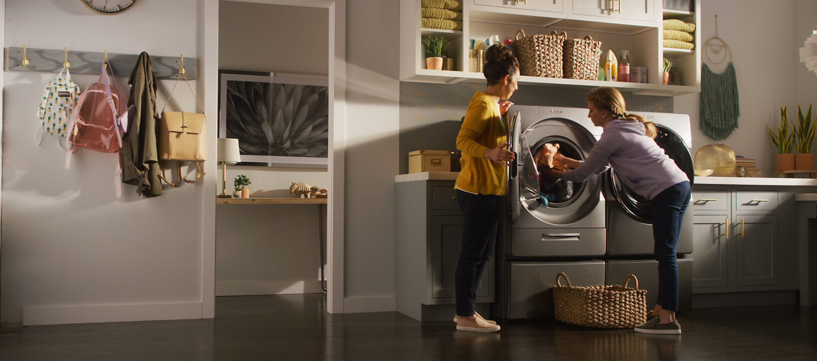 Young girl loading a washing machine in the laundry room while talking with her mother.