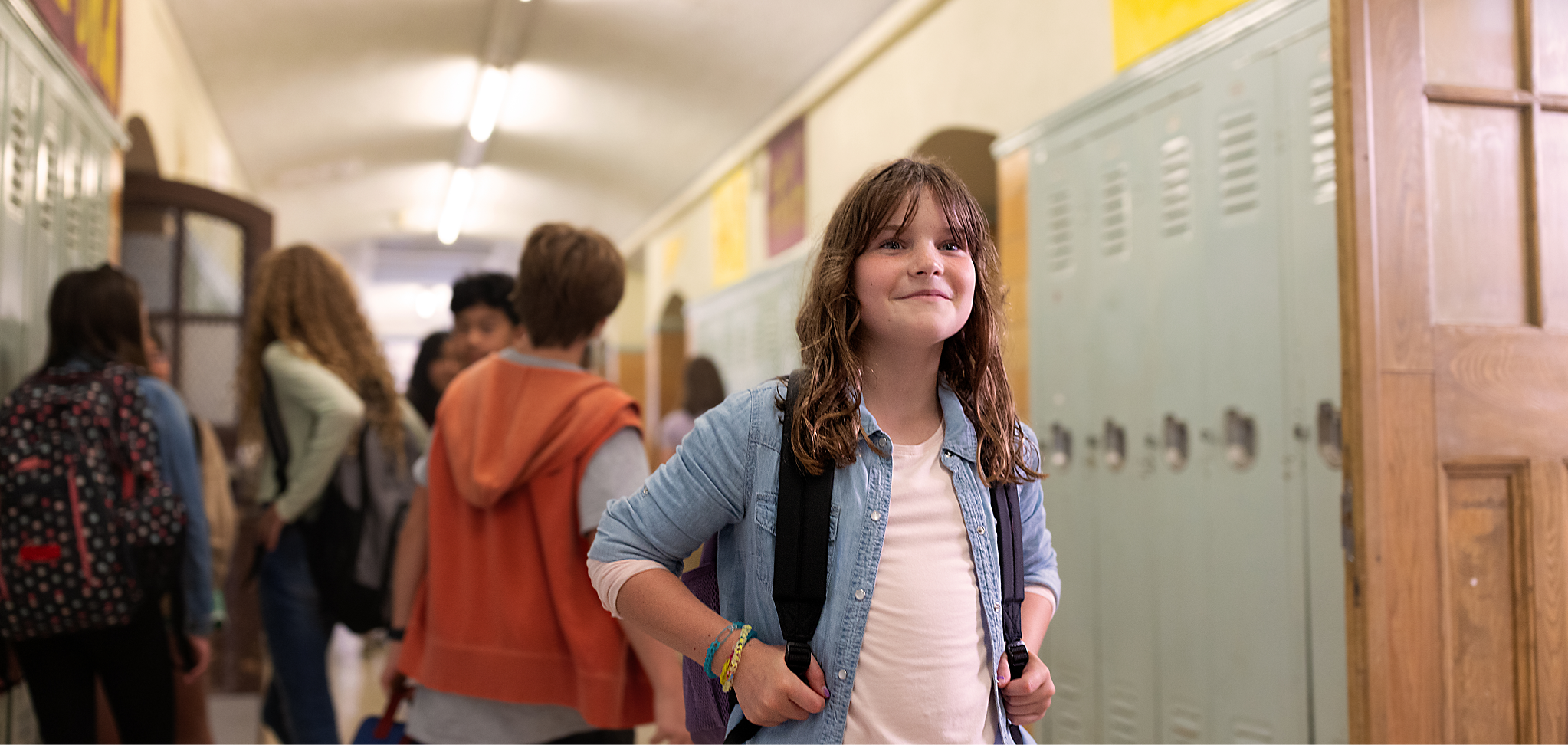 A smiling child in a school hallway with other kids behind them