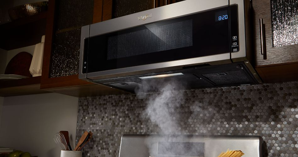 A Whirlpool over-the-range microwave. It is suctioning steam from the below range. The top of pasta cooking in a pot on the range is visible.