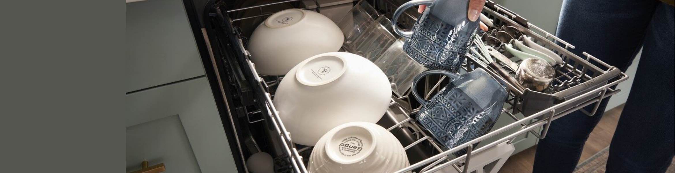 The top rack of a dishwasher pulled out. On the rack is a row of white bowls, a row of glasses. where a hand is removing a glass, and cutlery in a cutlery tray.