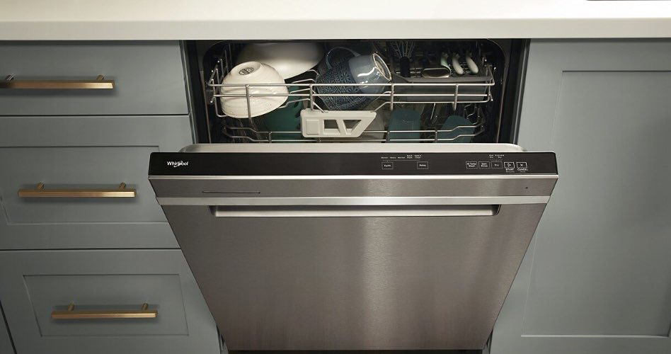 Between three gray drawers and a gray cabinet is a fully-integrated dishwasher with the door slightly open. The controls are visible on top of the dishwasher door. Inside on the top rack are white bowls, blue mugs and cutlery.