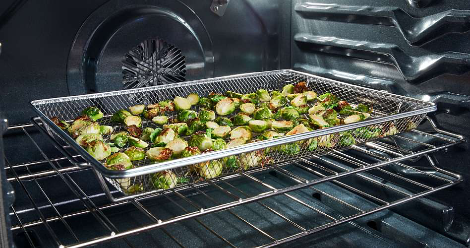 Inside an oven, Brussels sprouts cook in an air fry basket.