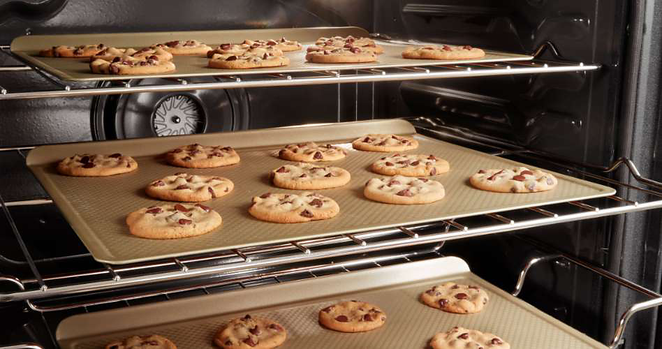 On each oven rack, a tray of cookies bake.