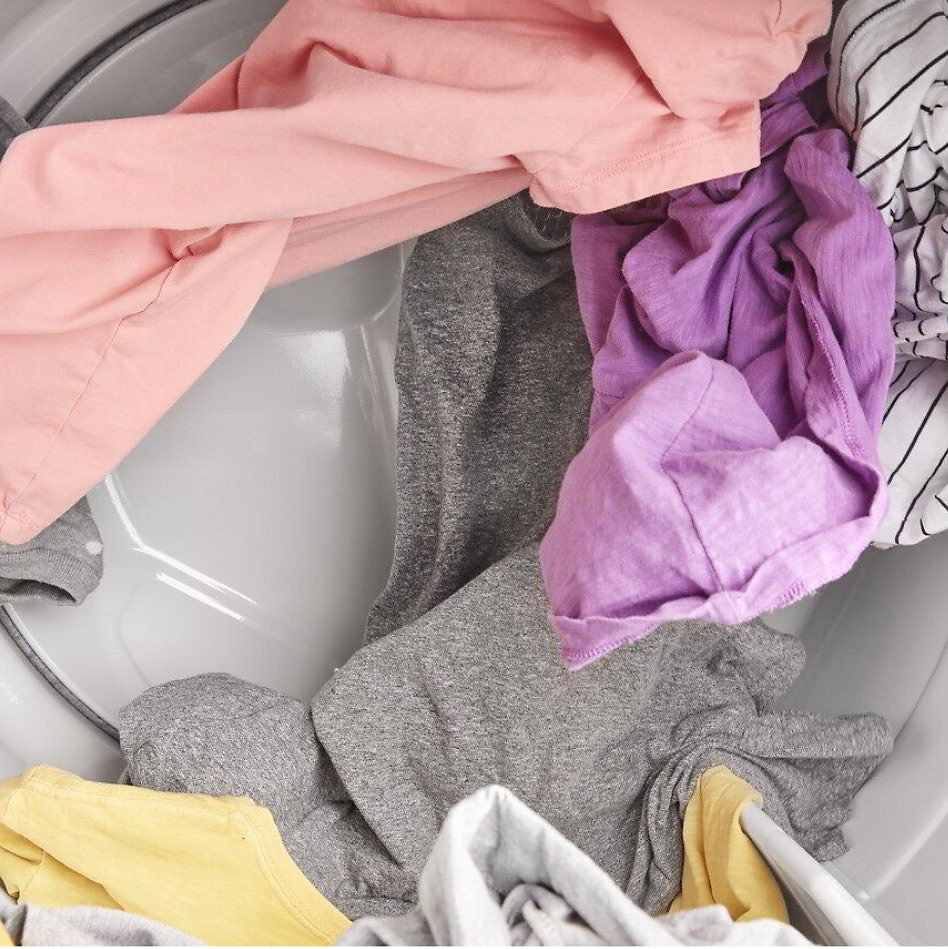 Inside a washing machine: pink, purple, grey and yellow articles of clothing.