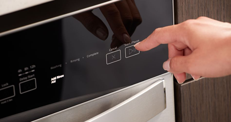 Someone about to press the "Start/Pause" button on a Whirlpool front-control dishwasher