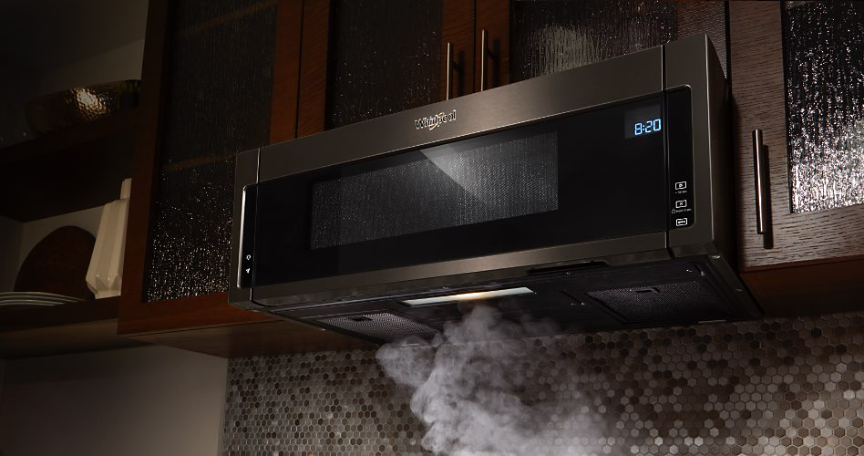An undercabinet microwave with a vent suctioning steam off a cooktop. Underneath the microwave is a backsplash with grey and white tiles