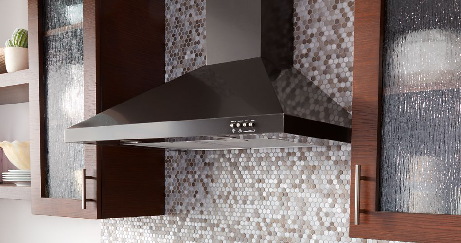 A black range hood in between two wood cabinets with glass doors. Behind the range hood and cabinets is a gray and white tile backsplash