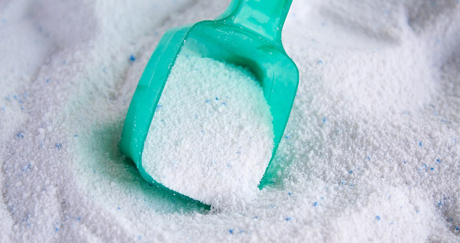 A green scooper scoops white detergent with blue specks