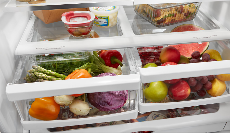 A variety of fruits and vegetables are seen inside the crisper drawers of a Whirlpool refrigerator