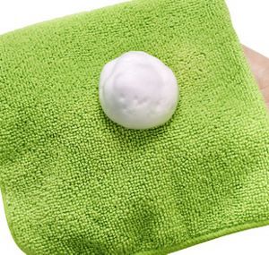 A hand holding a bright green microfibre cloth with some white cleaner on it