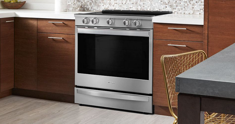 A Whirlpool stove in a kitchen with brown drawers and white countertops. In the foreground are a table and chair. 