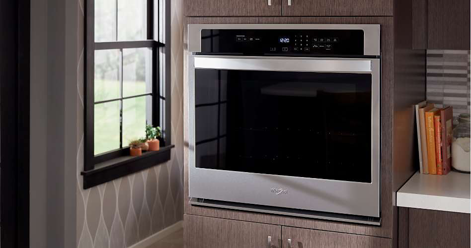 A stainless steel Whirlpool single wall oven recessed in a cabinet near a kitchen window