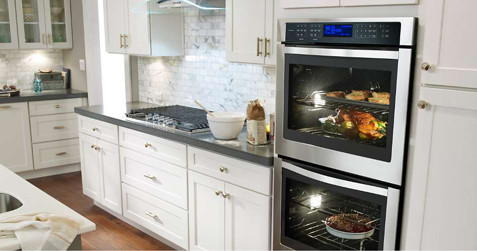 A stainless steel Whirlpool double wall oven built into a kitchen cabinet with white countertops