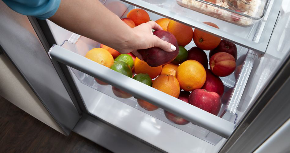 A variety of fruits are stored within the crisper drawer of a refrigerator
