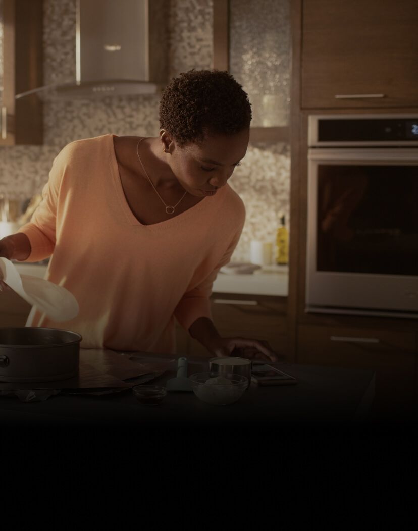 Woman in a kitchen following a recipe on her cell phone.