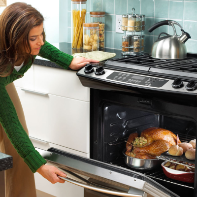 Woman closing door of oven filled with chicken, bread and other foods
