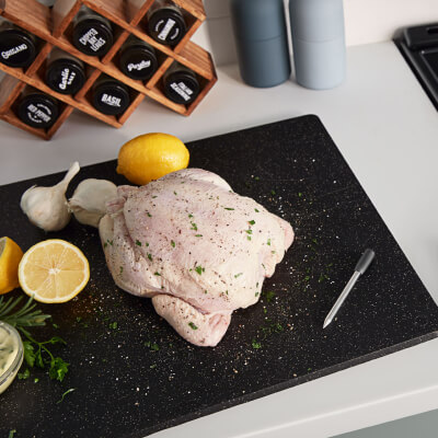 Whole raw chicken on black cutting board with ingredients