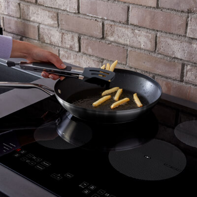 Person frying french fries in a skillet on an electric stovetop