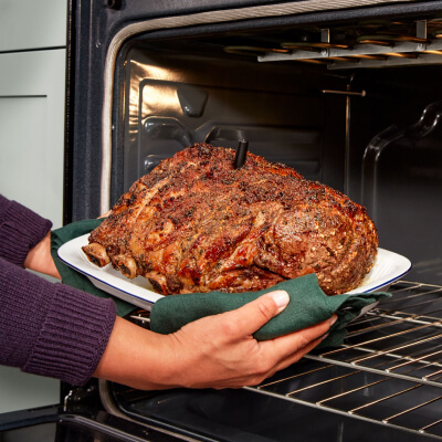 Person removing oven-roasted meat from the oven