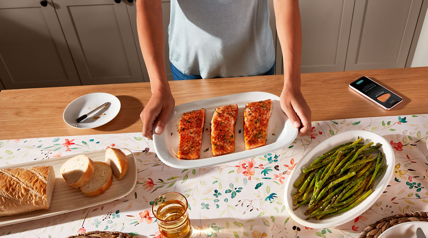 Birds-eye view of person holding platter with cooked salmon next to prepared bread and asparagus