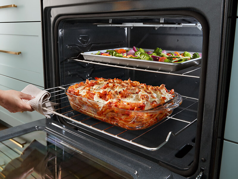 Person sliding out lower oven rack with lasagna on top 