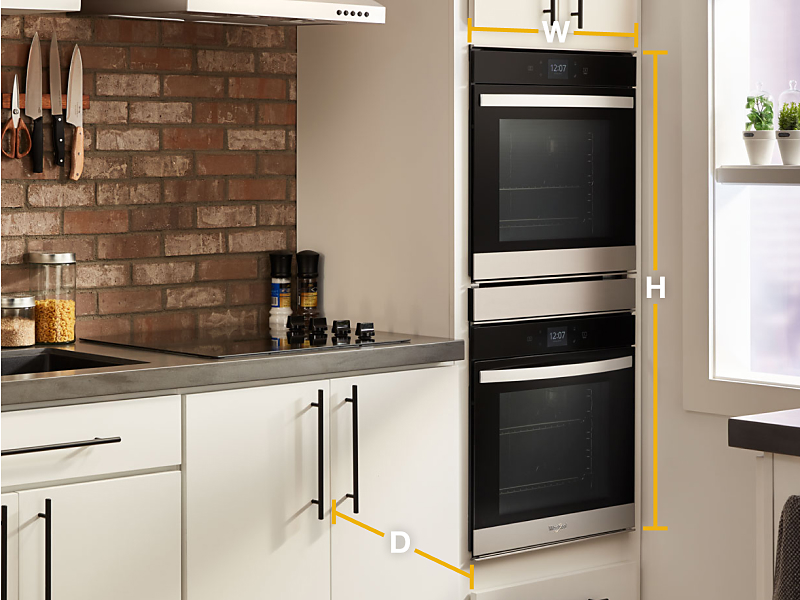Whirlpool® stainless steel double wall ovens set into white cabinets with diagram of width, height and depth