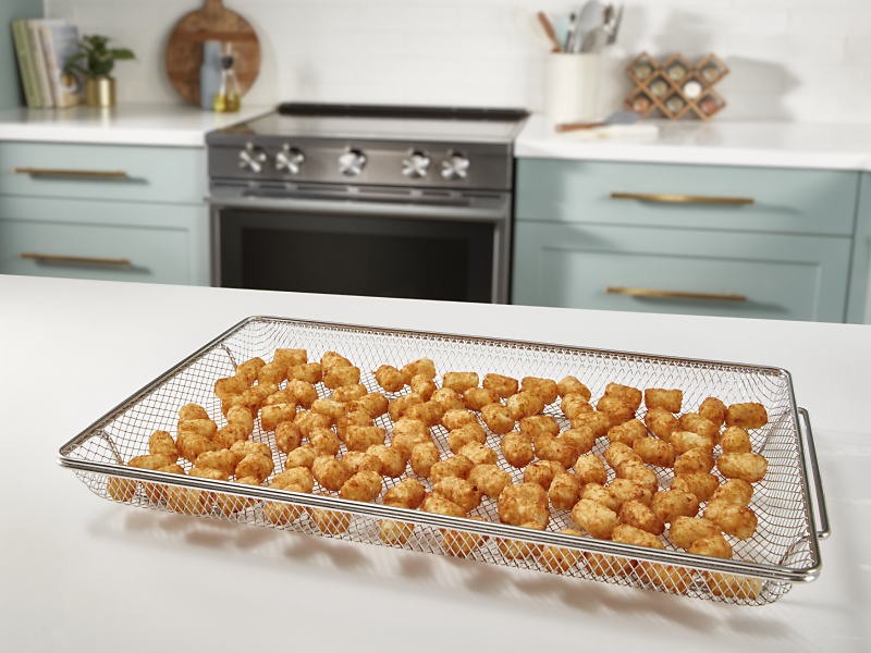 An air fry basket with tater tots sitting on a white countertop.